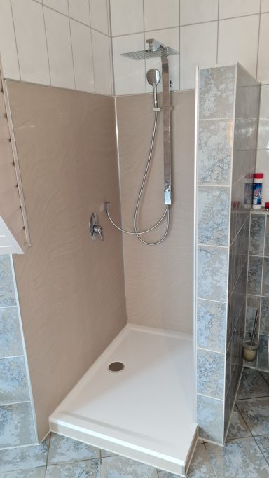 Moderne Dusche mit Duschkopf und im Duschbereich Wandverkleidung.