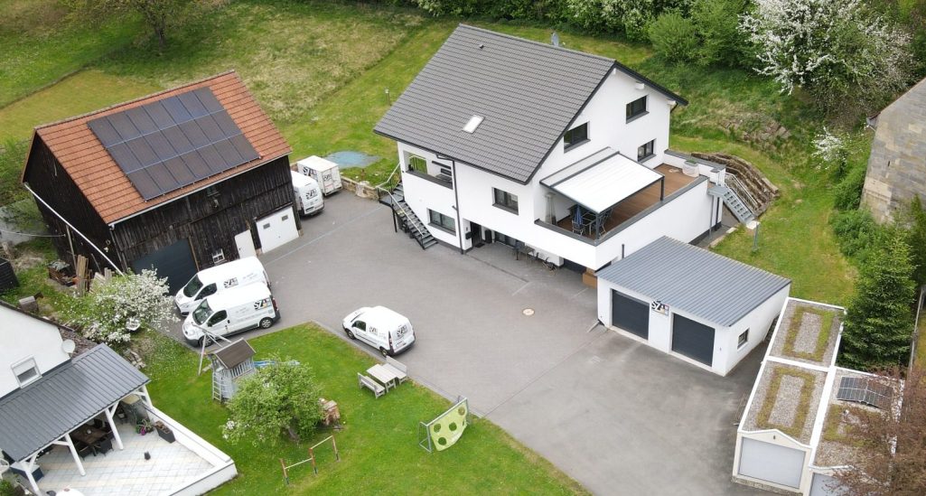 Schneebedeckte Landschaft mit einem Haus und Garagen, umgeben von Bäumen.